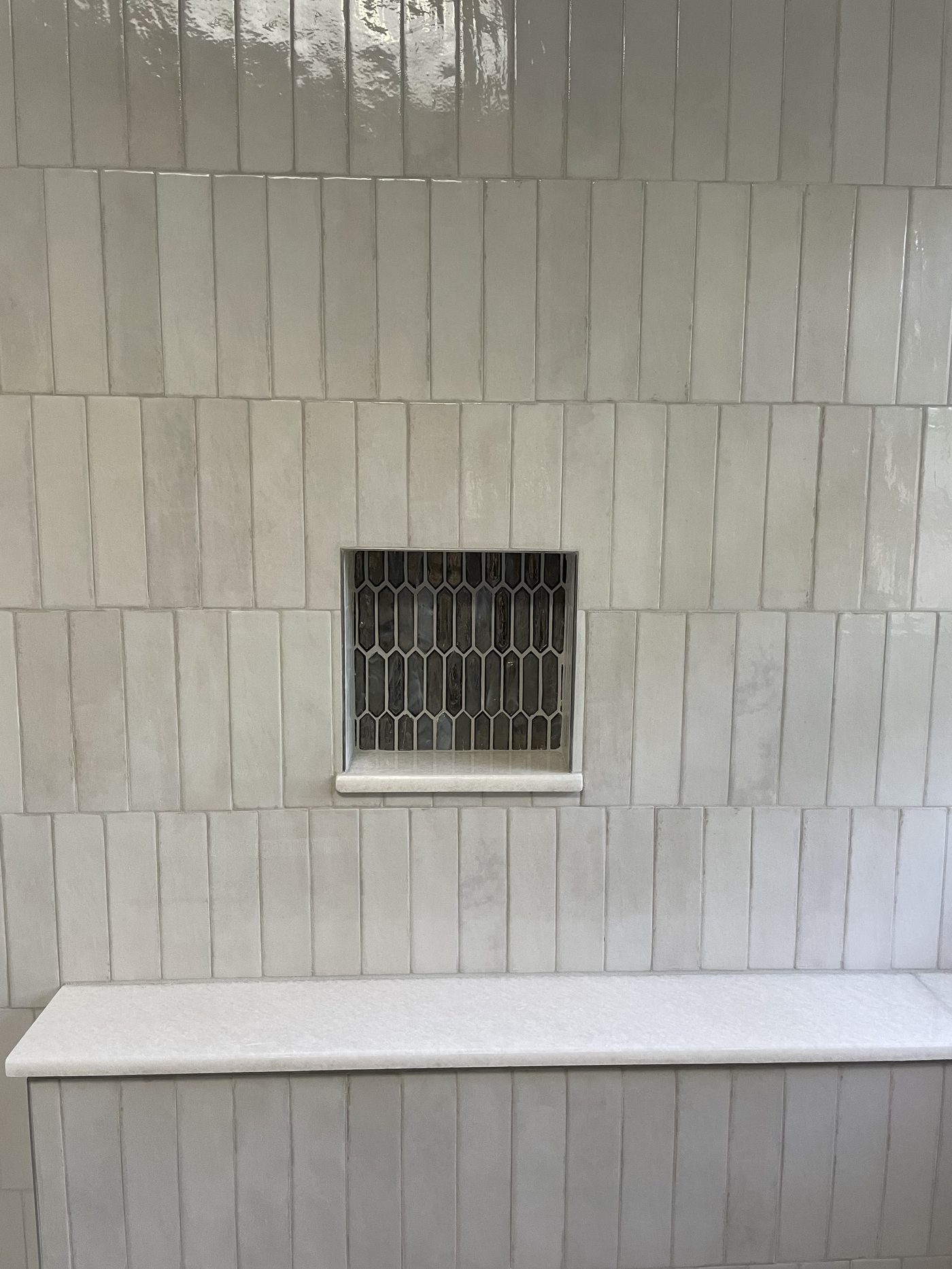 Walk-in shower with vertical white zellige stick tile walls, dark gold picket mosaic niche, and marble bench in Cuyahoga County